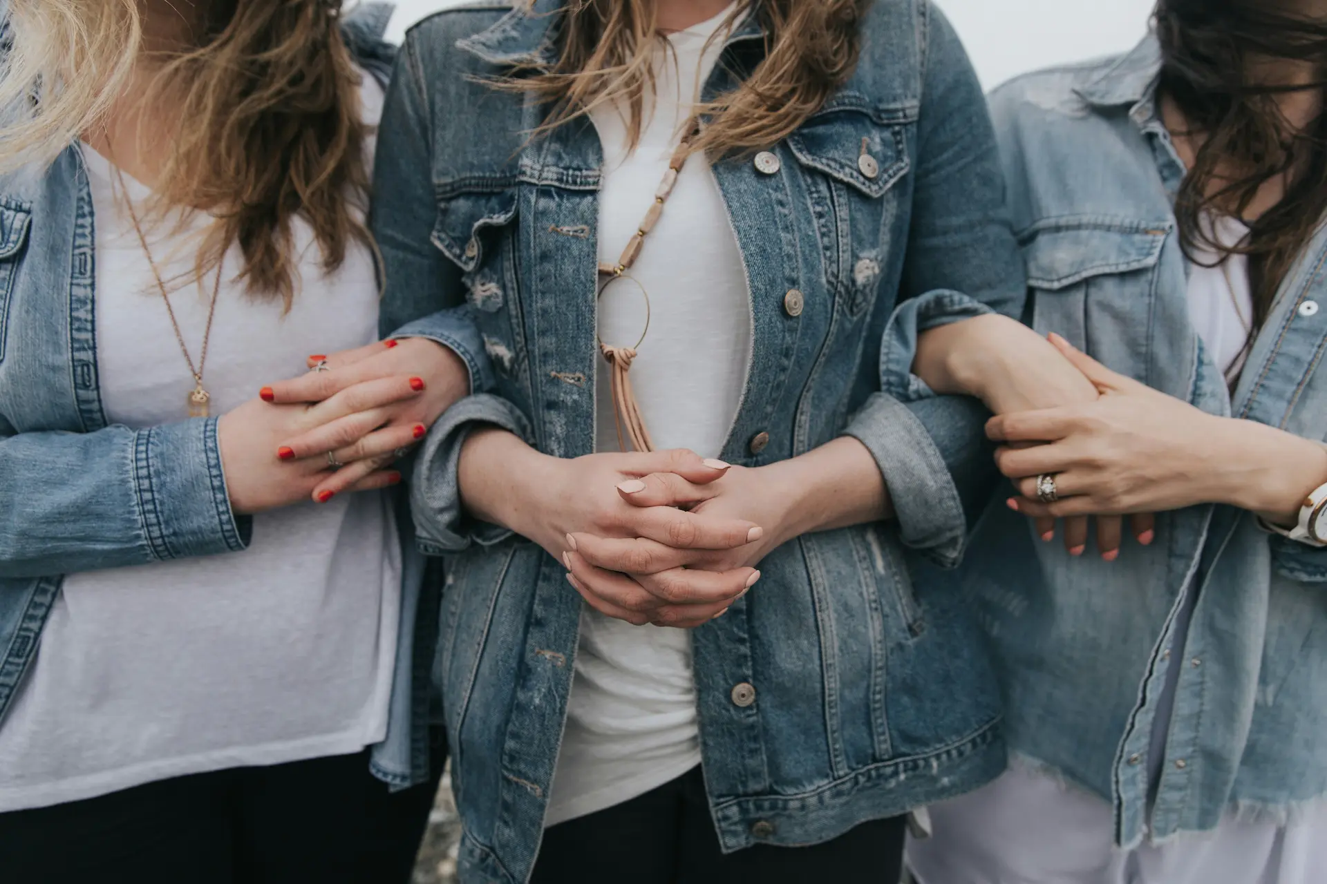 Three women wearing denim jackets and white t-shirts, linking arms together.