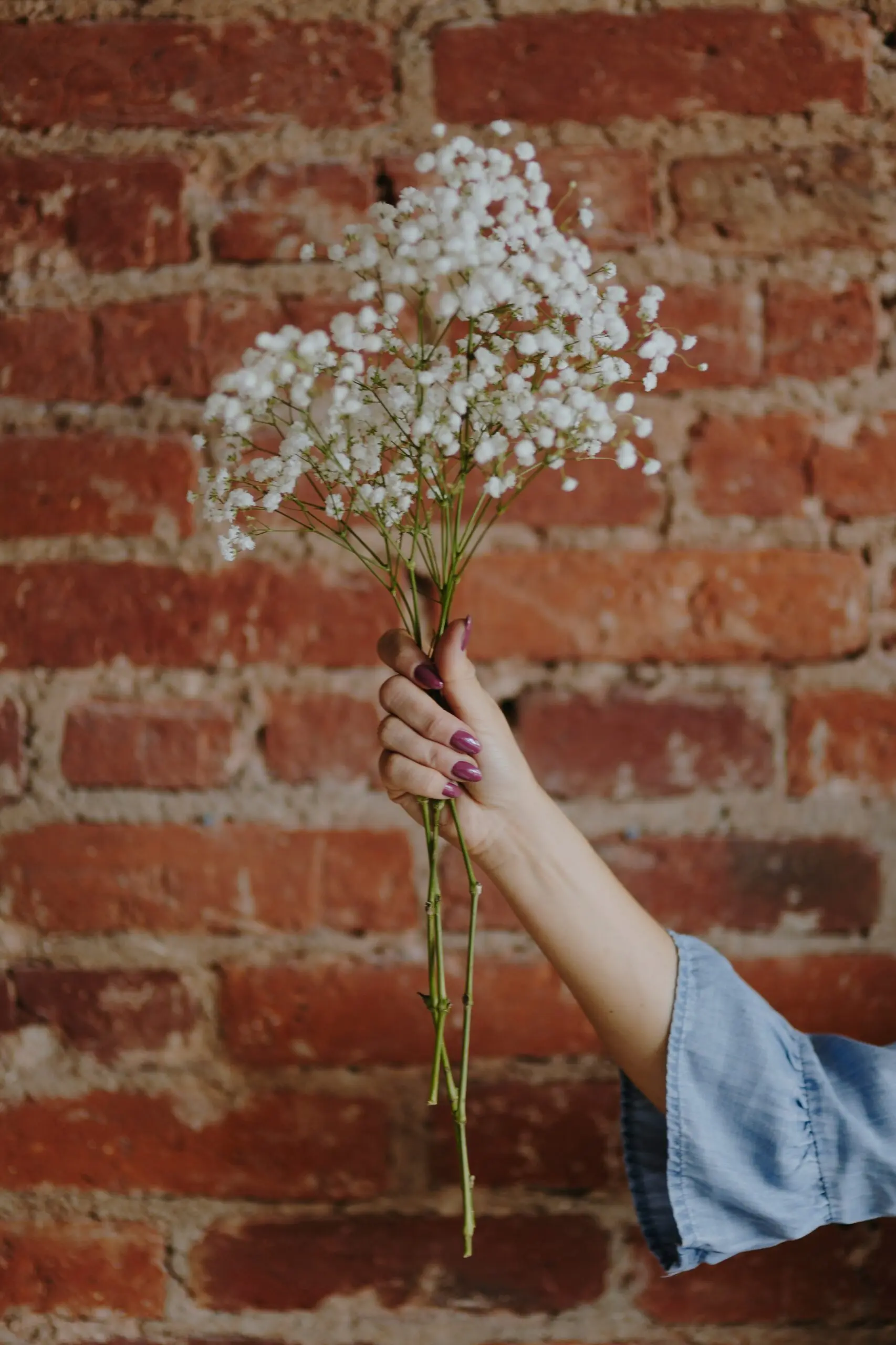 woman holds boquet of flowers in front of brick wall