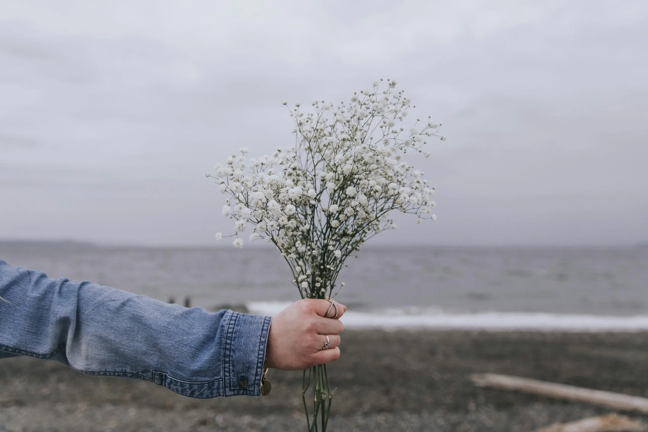 a woman holds some baby's breath flowers on the beach