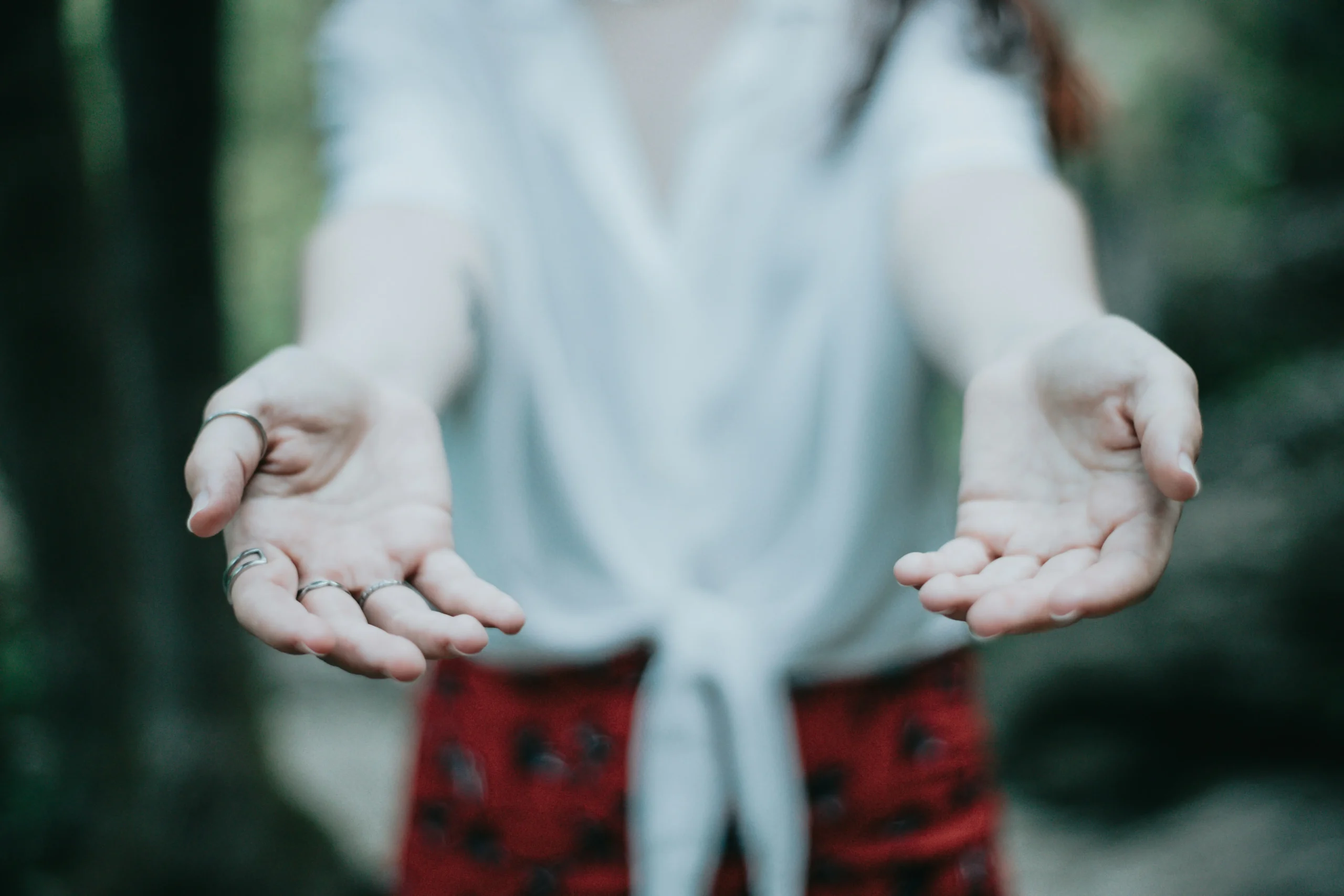 A woman among the greenery with two hands outstretched.