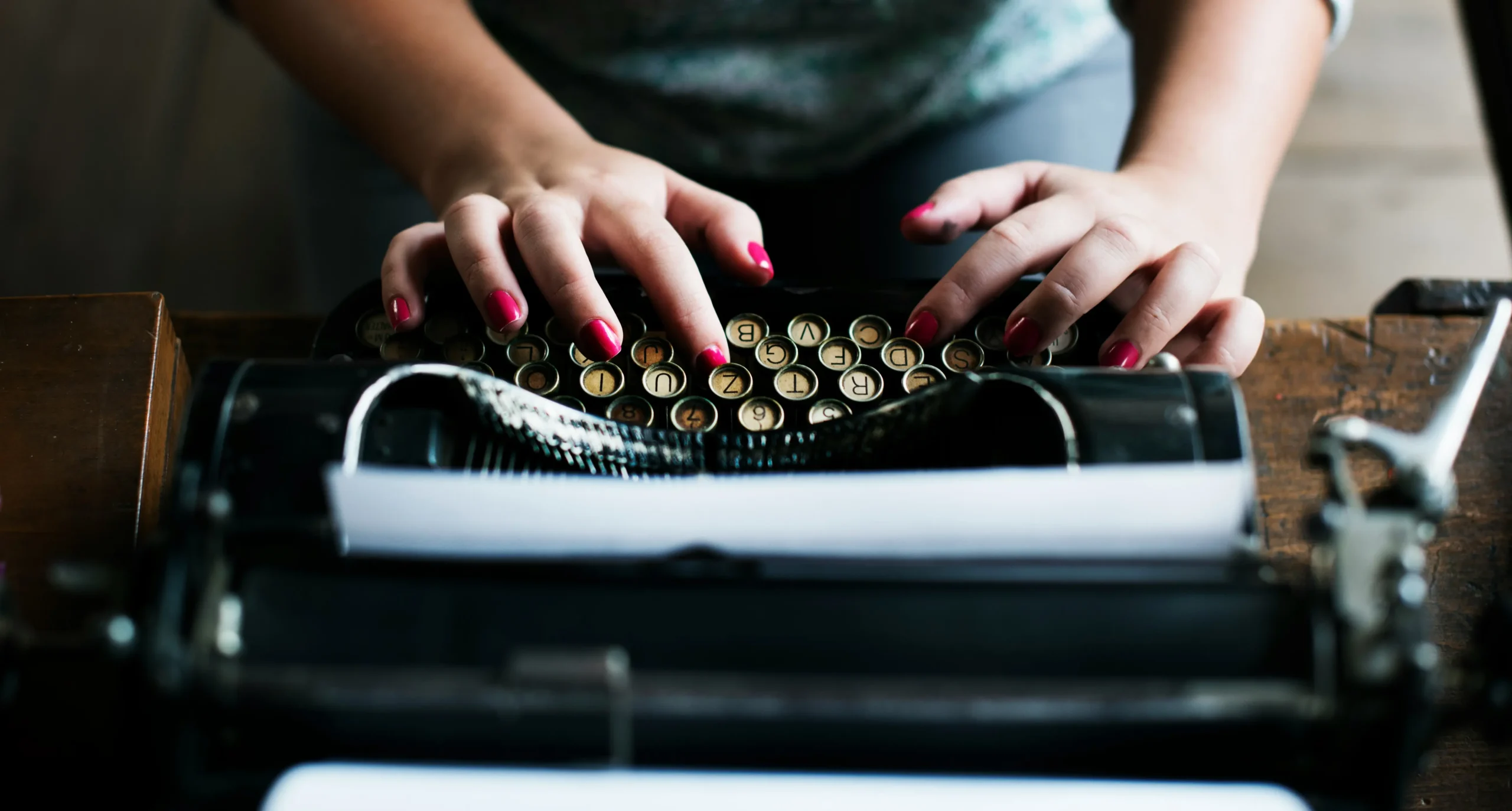 Blog A woman typing on a typerwriter. She has bold red nails, and is writing empowering blogs.